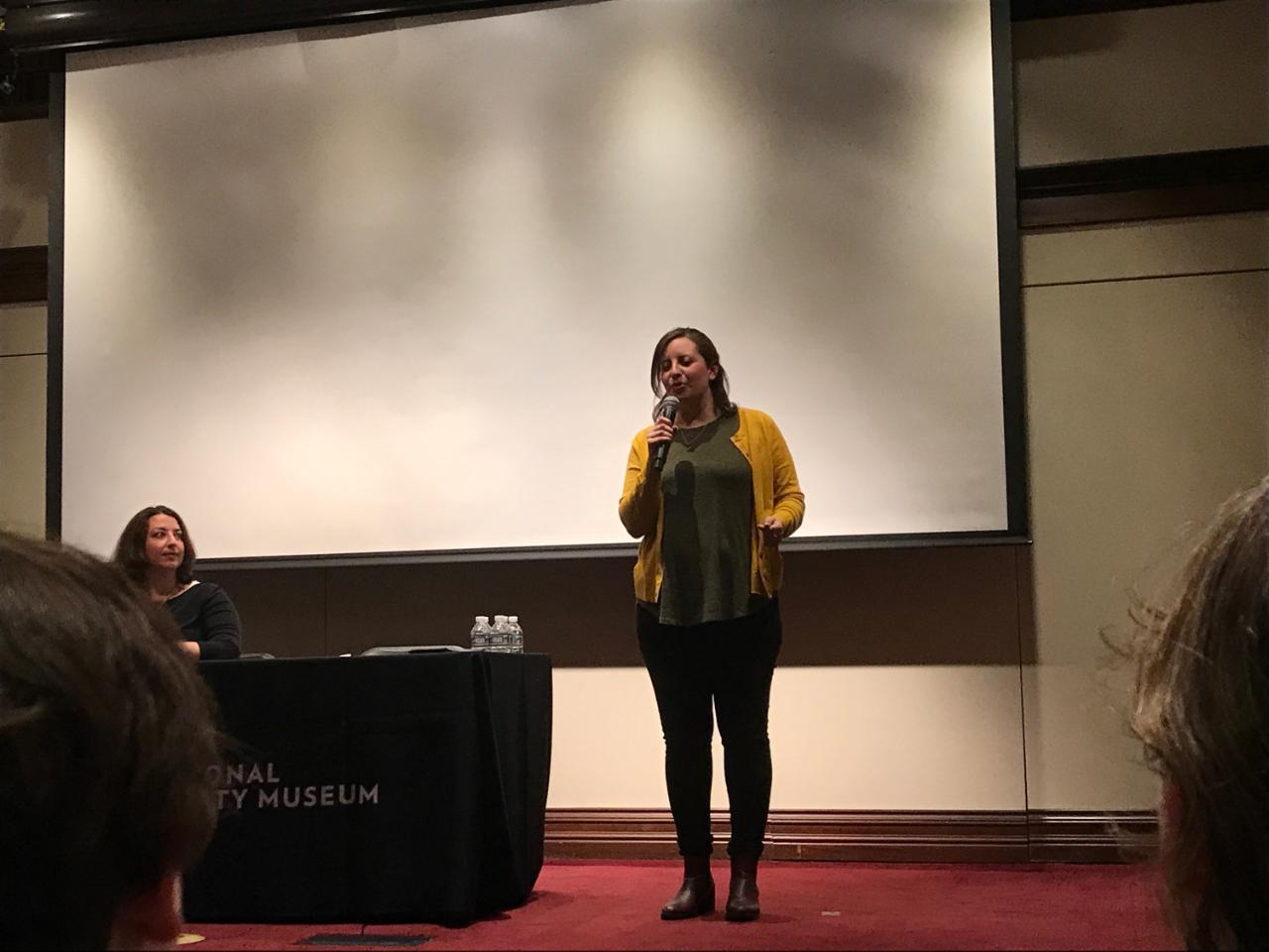 Alanna Raffel standing on a stage talking into a microphone